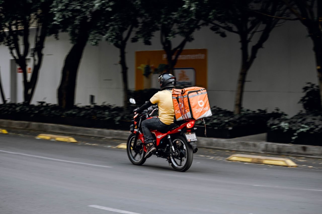 The Art of Drawing Readers In: Your attractive post title goes here A delivery man riding a motorcycle with a thermal bag on a city street during the day.