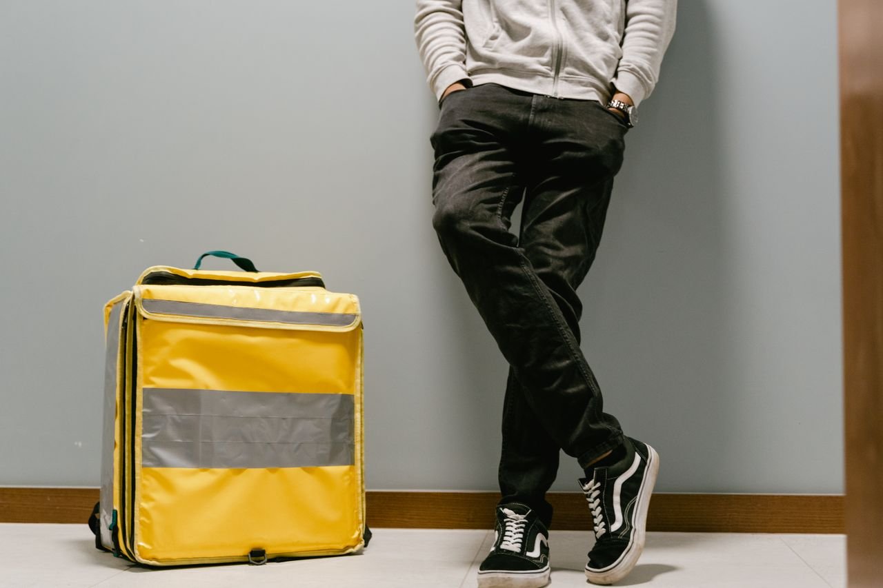 Mastering the First Impression: Your intriguing post title goes here Casual food delivery courier leaning against a wall with a yellow thermal bag.